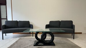Een moderne woonkamer met twee donkergrijze banken, een glazen salontafel met zwart onderstel, en een grijze vloerkleed.