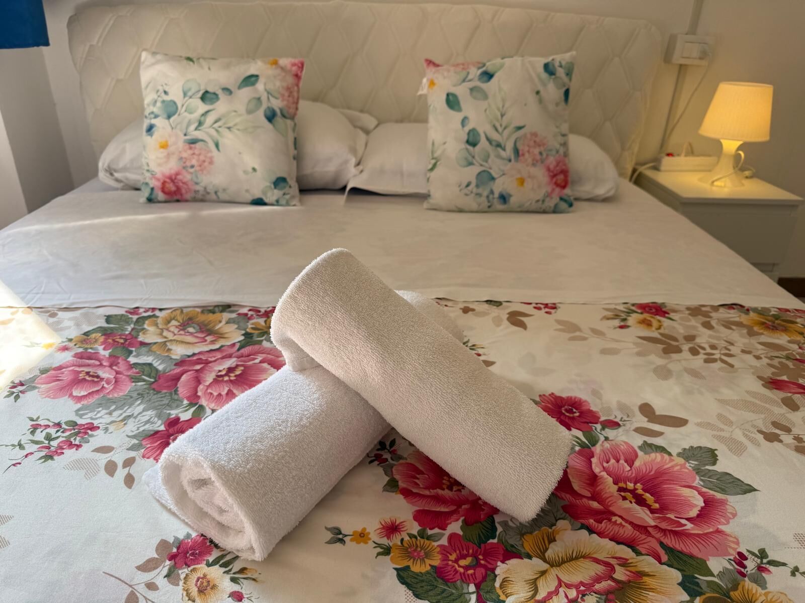 A neatly made bed with floral bedding, two pillows, and a folded towel on the bed.