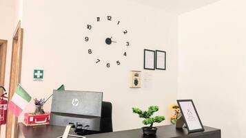 Una mesa de recepción con una computadora HP, un reloj, certificados enmarcados y una pequeña planta en maceta.