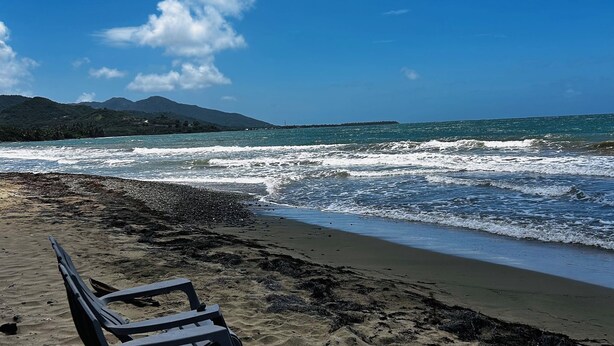 Una playa con una fila de sillas de plástico vacías mirando al océano.
