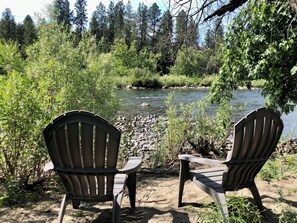 Twee Adirondack-stoelen gericht op een rivier, met groene begroeiing eromheen.