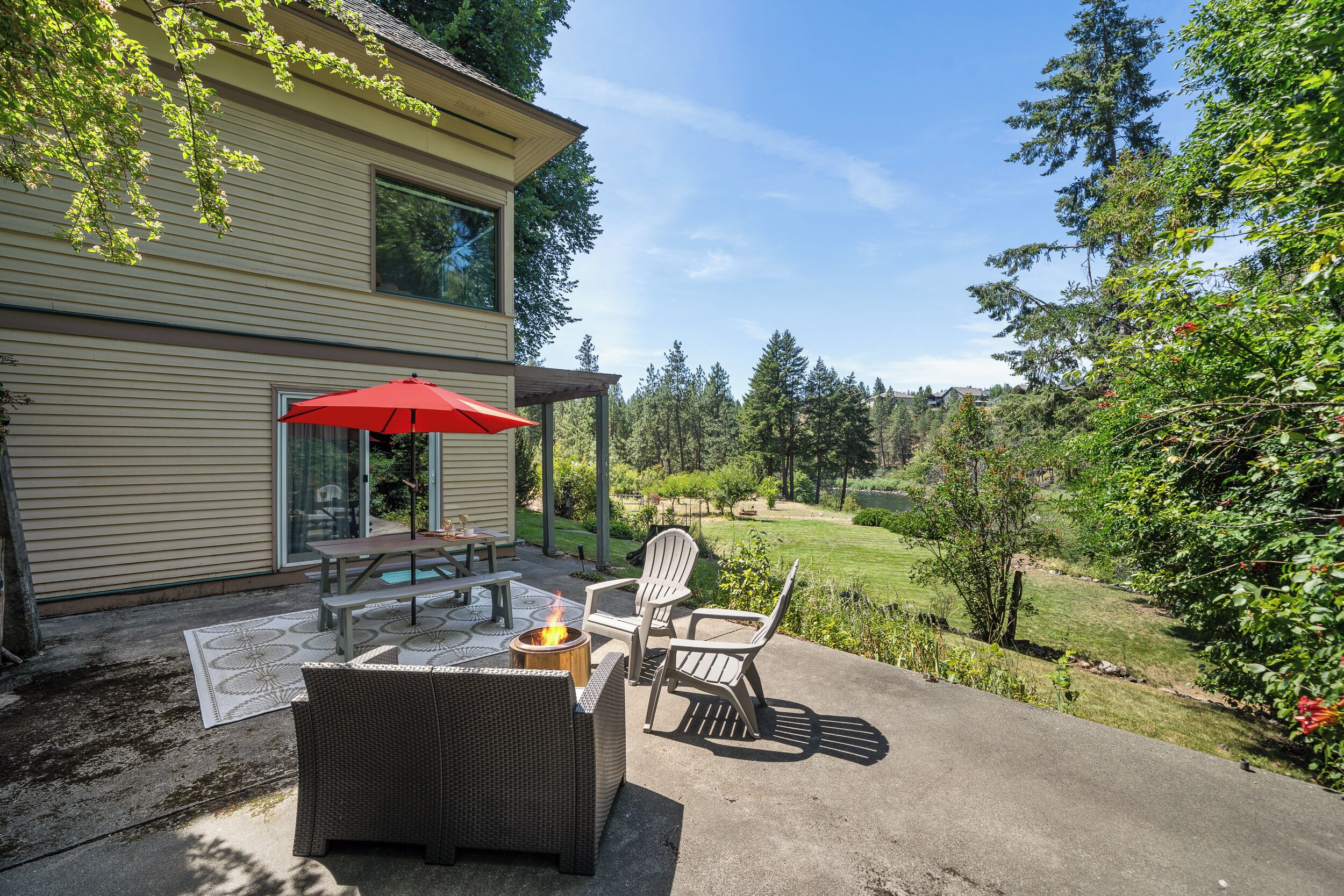 A patio with wicker furniture, a red umbrella, and a fire pit.