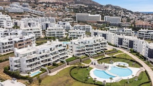 Et moderne boligkompleks med flere lejlighedsbygninger, en central swimmingpool og grønne områder omkring.