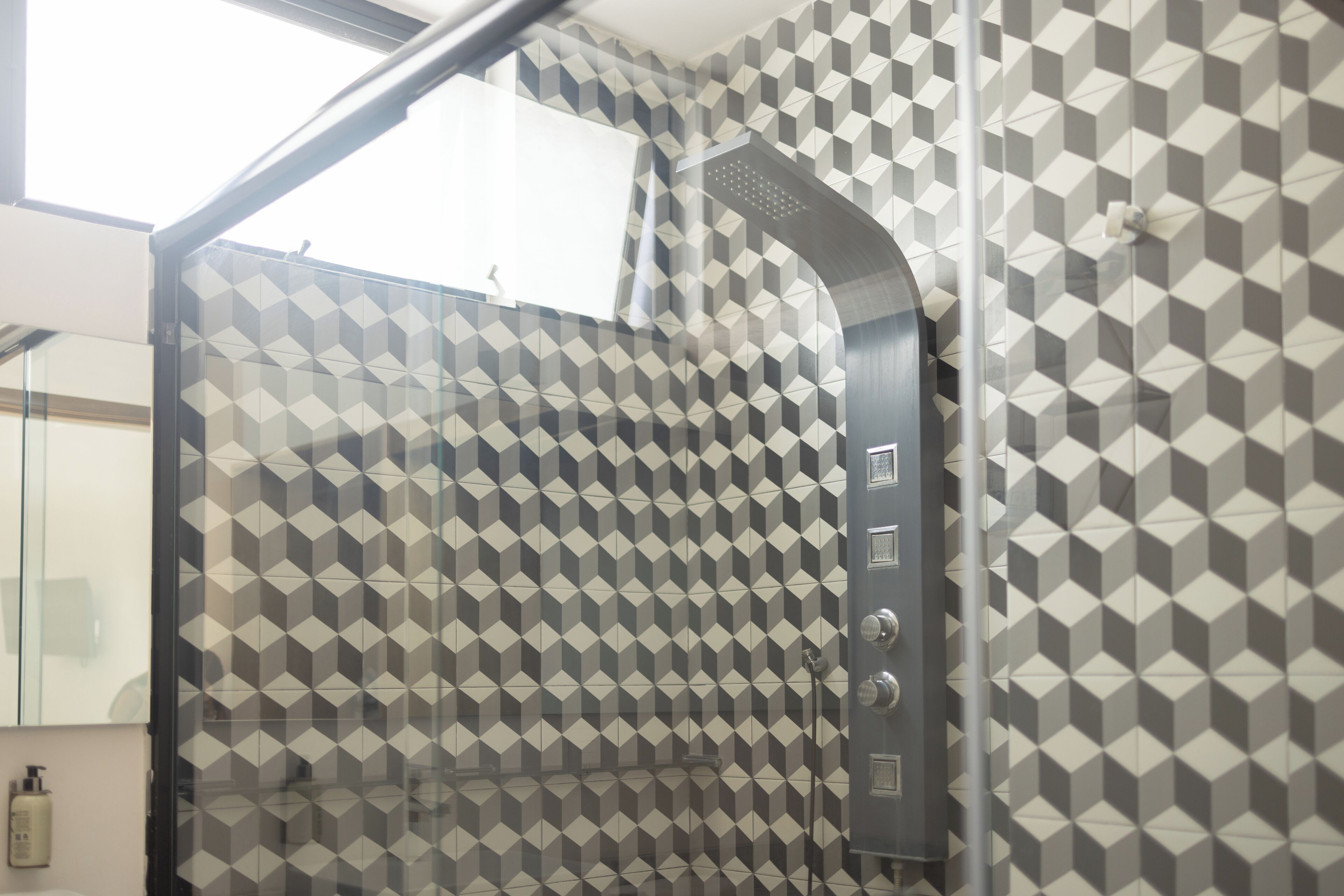 Un baño moderno con un revestimiento mural de diseño geométrico, una cabina de ducha de vidrio y un secamanos visible.