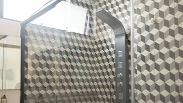 Un baño moderno con un revestimiento mural de diseño geométrico, una cabina de ducha de vidrio y un secamanos visible.