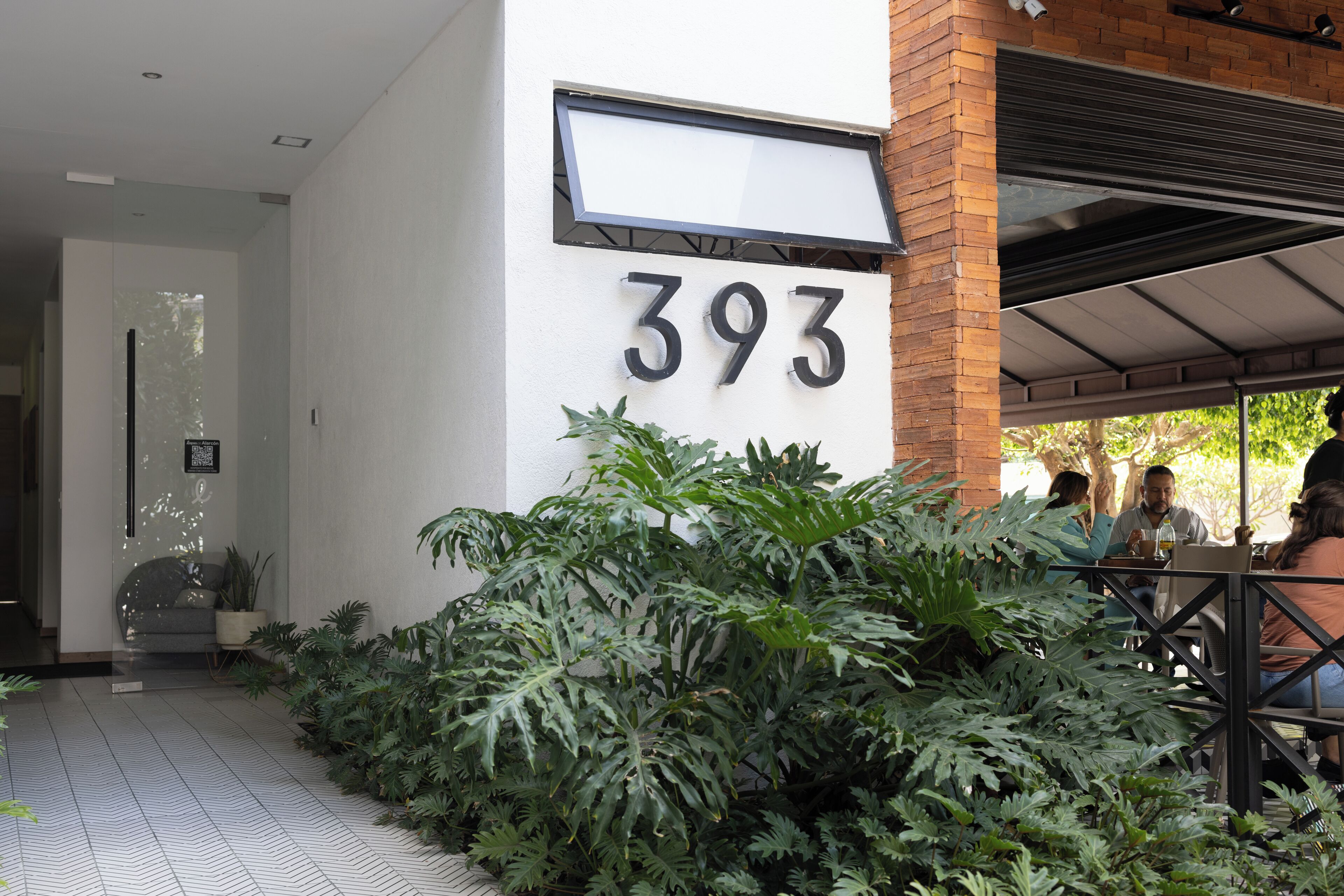 Ingresso di un edificio con il numero 393, una zona salotto esterna coperta e vegetazione lussureggiante.