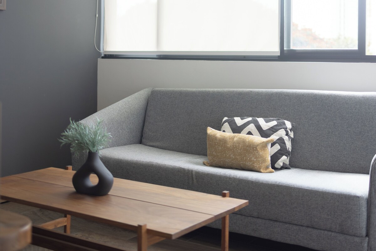 A modern living room with a grey sofa, a wooden coffee table, and a potted plant.