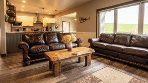 A spacious living room with two leather sofas, a wooden coffee table, and a large window offering a view of the outdoors.