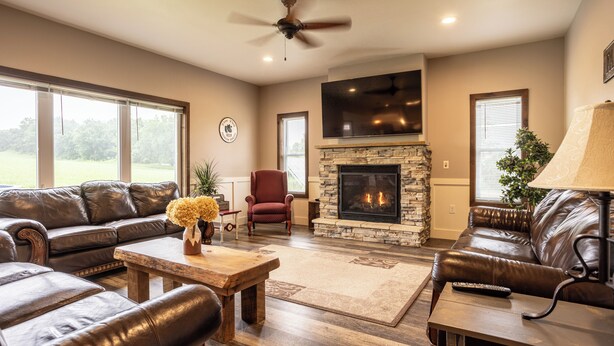A living room with leather sofas, a fireplace, a television, and a ceiling fan.