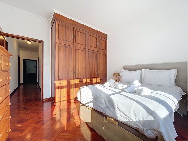 Une chambre avec une armoire en bois, un lit avec du linge de lit blanc et une commode en bois.