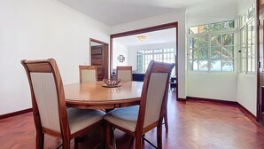 Un comedor con una mesa de madera y cuatro sillas, un espejo grande, y vistas a otra zona de comedor a través de una puerta de cristal.