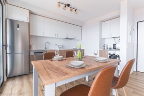 Una cocina moderna con armarios blancos, un refrigerador de acero inoxidable y una mesa de comedor de madera para cuatro comensales.