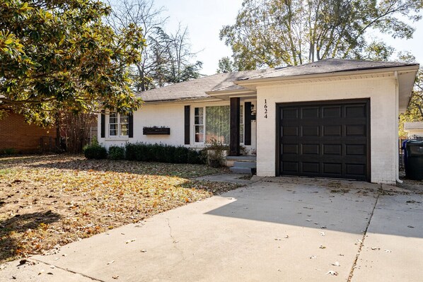 A single-story house with a garage, a front porch, and a small yard with fallen leaves.