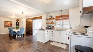 A modern kitchen with white cabinets, a central island, and a dining area with blue chairs. - Magnolia - 4 Bedroom 2 bath & pets allowed (Norman)