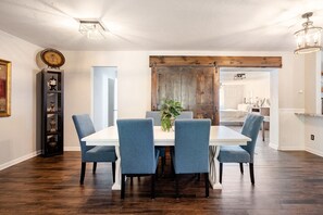 A dining room with a white table and blue chairs, wooden flooring, and a rustic wooden door.