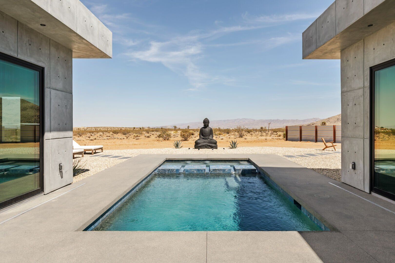 A modern pool area with a Buddha statue, surrounded by desert landscape and clear skies.