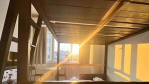 A room with a bunk bed, a desk, and a chair. There is a window with a view of buildings outside. - Aelia Sky View Loft & Rooftop Acropolis View (Athens)