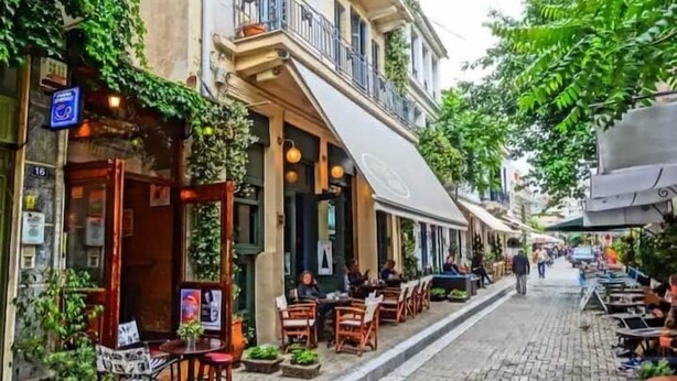 A narrow cobblestone street lined with outdoor seating and greenery, suggesting a quaint, possibly historic urban setting. - Aelia Sky View Loft & Rooftop Acropolis View (Athens)