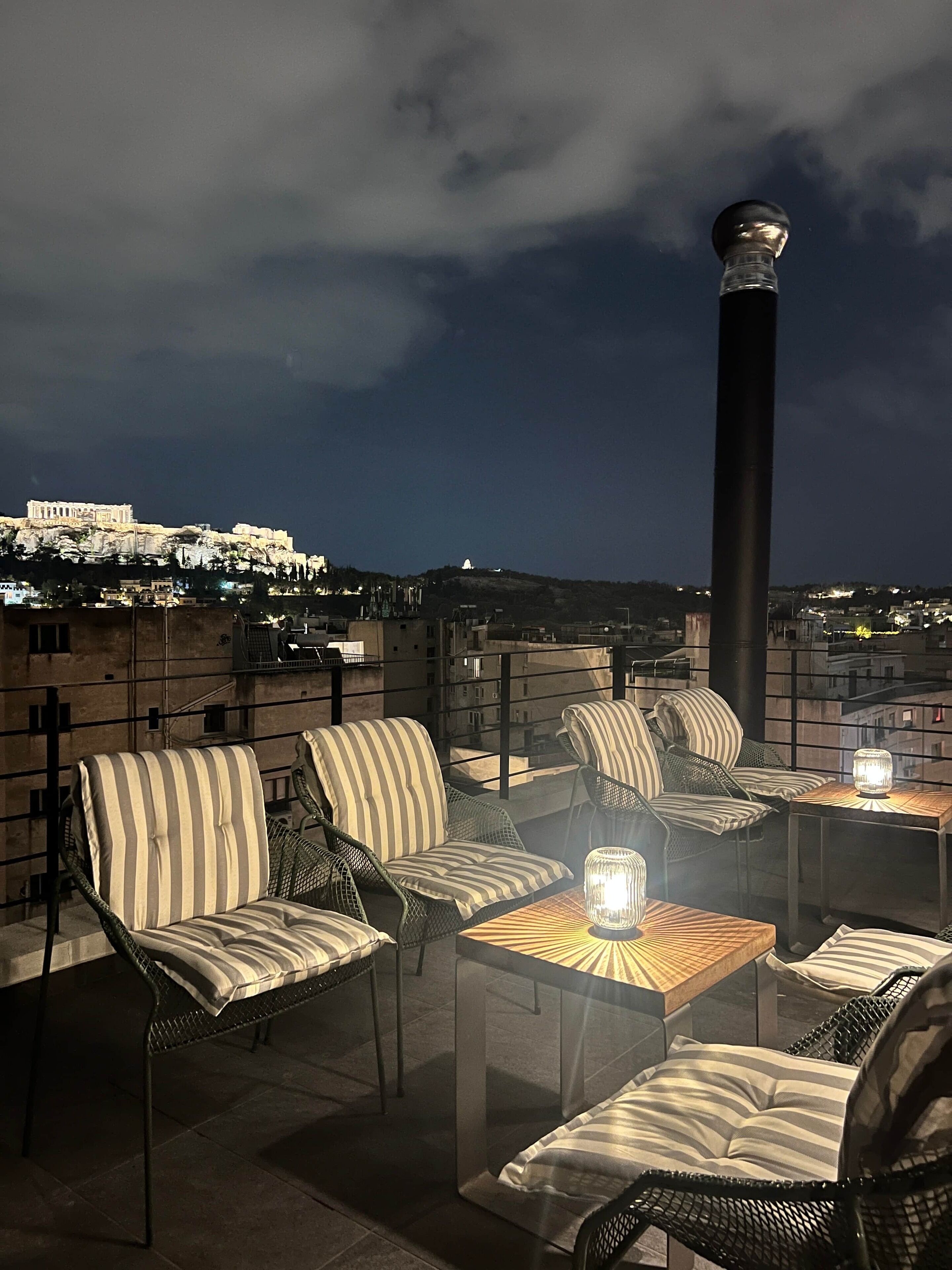 A rooftop terrace with outdoor seating and a view of the Acropolis.