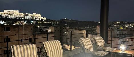 A rooftop terrace with outdoor seating and a view of the Acropolis.