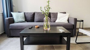 A modern living room with a grey sofa, a coffee table, and a vase with green plants. - Aelia Loft with Terrace & Rooftop Acropolis View (Athens)