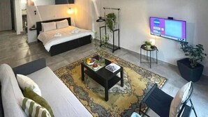 A modern hotel room with a bed, sofa, coffee table, TV, and a small side table with a plant. - Aelia Loft with Terrace & Rooftop Acropolis View (Athens)
