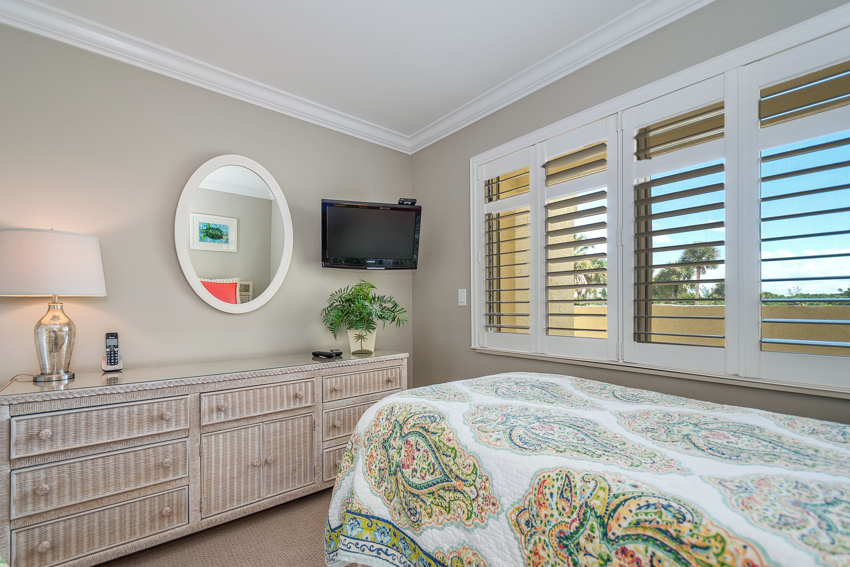 Un dormitorio con cama, cómoda, televisor y ventana con persianas.