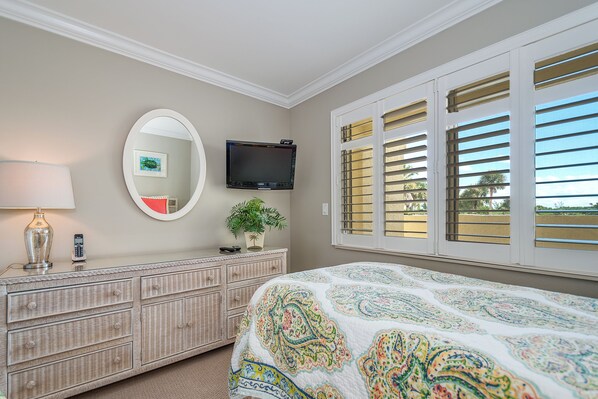 Un dormitorio con cama, cómoda, televisor y ventana con persianas.