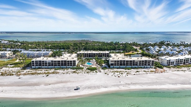 Vista aérea de un hotel costero con varias construcciones, una playa arenosa y una vista despejada del océano.