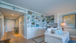 Un salón amplio con un sofá blanco, una estantería grande llena de objetos decorativos y un mapa en la pared.