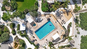 Vista aérea de un resort con una piscina central, rodeado de palmeras y zonas de descanso.