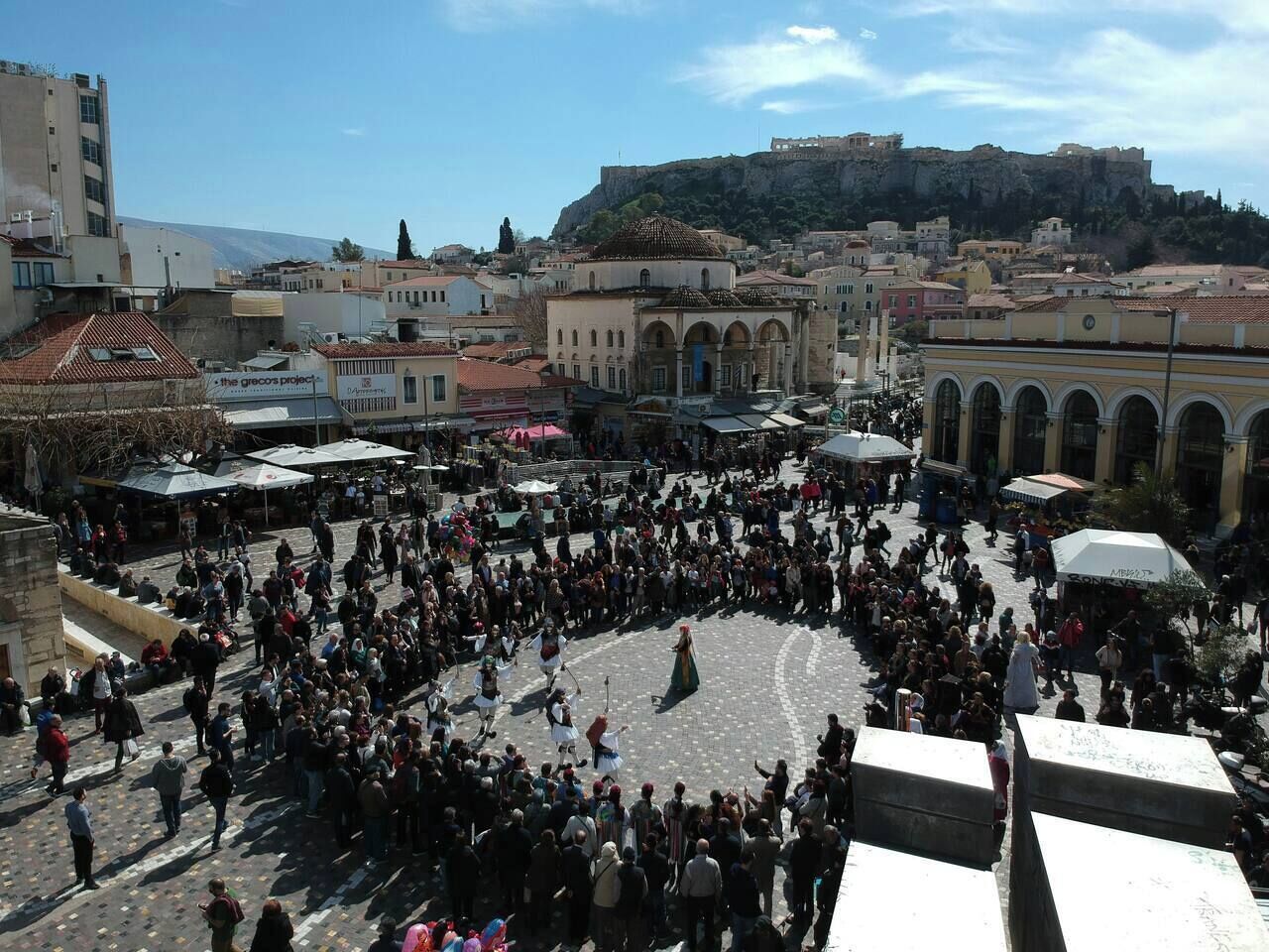 A crowded square with historical architecture, including a prominent building with arches and a large open space in the center.