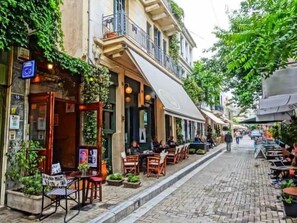 A narrow cobblestone street lined with outdoor seating and greenery, suggesting a quaint, possibly historic urban setting. - ÆLIS Suite with Terrace & Rooftop Acropolis View (Athens)