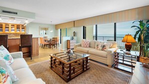 Ein geräumiges Wohnzimmer mit großem Fenster zum Meer, einer gemütlichen Sitzecke und einer Küche im Hintergrund.