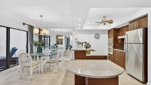 A modern kitchen with a central island, stainless steel appliances, and a dining area with wicker chairs.