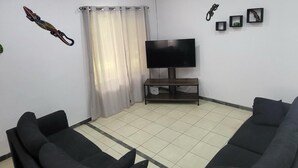 A living room with two black sofas, a flat-screen TV on a stand, a ceiling fan, and a curtain. - Villa Milagro (Provincia de Puntarenas)
