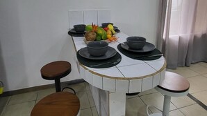 A kitchen with a round table, two stools, a clock, and a fruit bowl. - Villa Milagro (Provincia de Puntarenas)