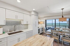 Eine Küche mit weißen Schränken, einer Holzausziehtheke und Blick aufs Meer vom Balkon.