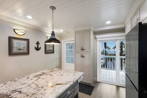 A kitchen with a marble countertop, pendant lighting, and a view to a balcony with outdoor scenery.