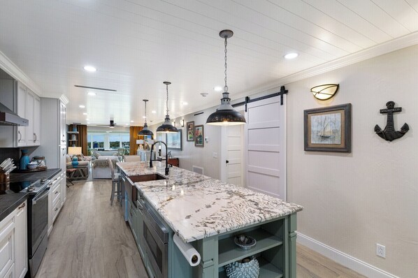 A spacious kitchen with a large island, pendant lighting, and a view to the living area.