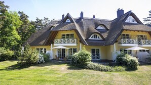 A yellow house with a thatched roof, a balcony, and a well-maintained garden. - Souterrain Ferienwohnung in Dierhagen (Ostseebad Dierhagen)