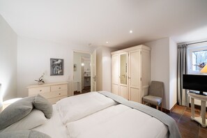 Ein Hotelzimmer mit Bett, Sessel, Fernseher, Kleiderschrank und einem durchgegangenen Tür sichtbaren Badezimmer.