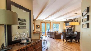 A spacious living area with a wooden floor, a sofa, a dining table with chairs, and a kitchen area with a stone fireplace.