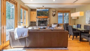 A cozy living room with a stone fireplace, a large sofa, and a dining area with a table and chairs.