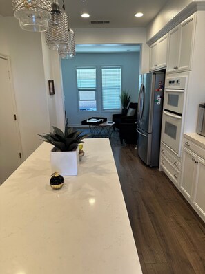 Una cocina moderna con una isla central, muebles blancos y un refrigerador de acero inoxidable.