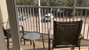 A balcony with a table and chairs, a view of parked cars and trees. - Charming 1-bedroom condo in lovely Bonita Springs with WiFi, AC pool. And tennis (Bonita Springs)