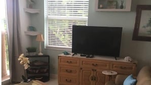 A living room with a sofa, ottoman, and a television on a wooden cabinet. - Charming 1-bedroom condo in lovely Bonita Springs with WiFi, AC pool. And tennis (Bonita Springs)