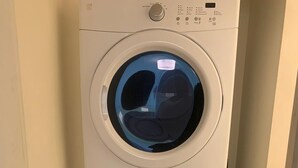 A stacked washer and dryer unit in a corner with a blue detergent bottle beside it.