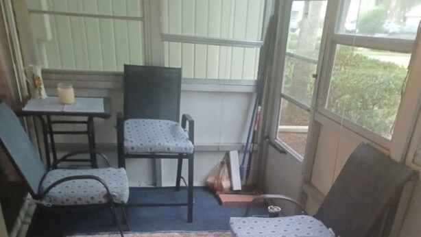 A small, enclosed porch area with a patterned rug, two chairs, a table, and a window.
