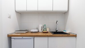 A compact kitchen with white cabinets, a wooden countertop, a sink, a dishwasher, and a kettle. - Silesian Charm Kozielska 1 Studio (Katowice)